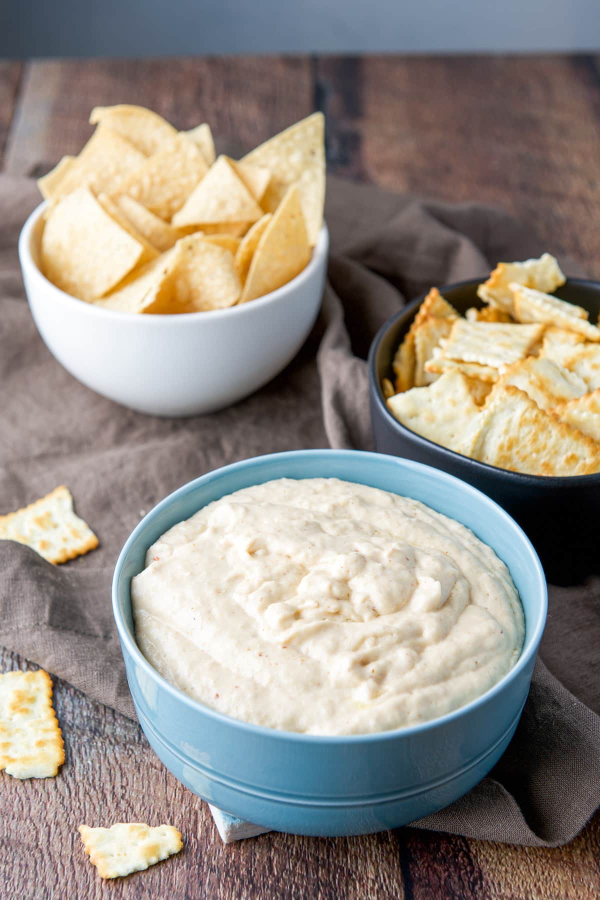 Chips in bowls behind the dip in a blue bowl on a wooden table