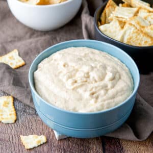 Blue bowl filled with the creamy dip with chips in bowls and on the table