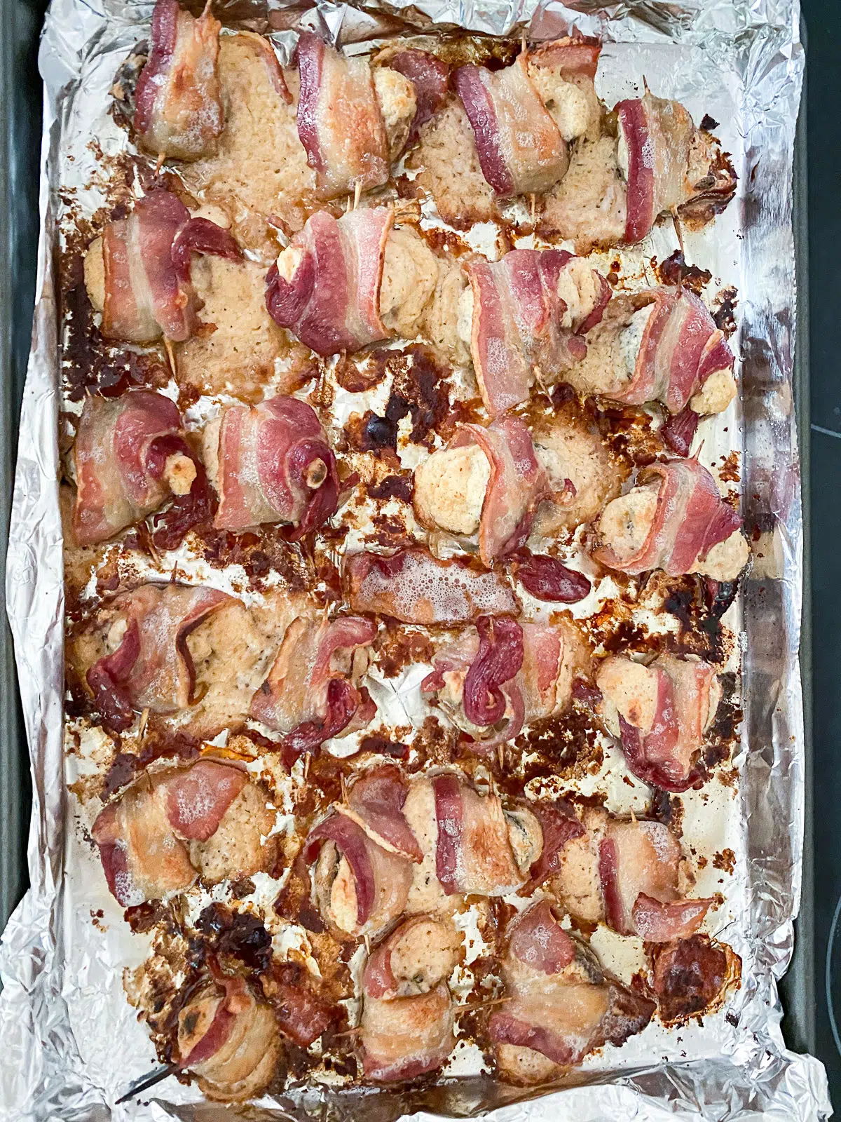 Foil pan with cooked bacon wrapped mushrooms on it