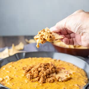 square photo of a hand holding a chip with the cheese dip on it