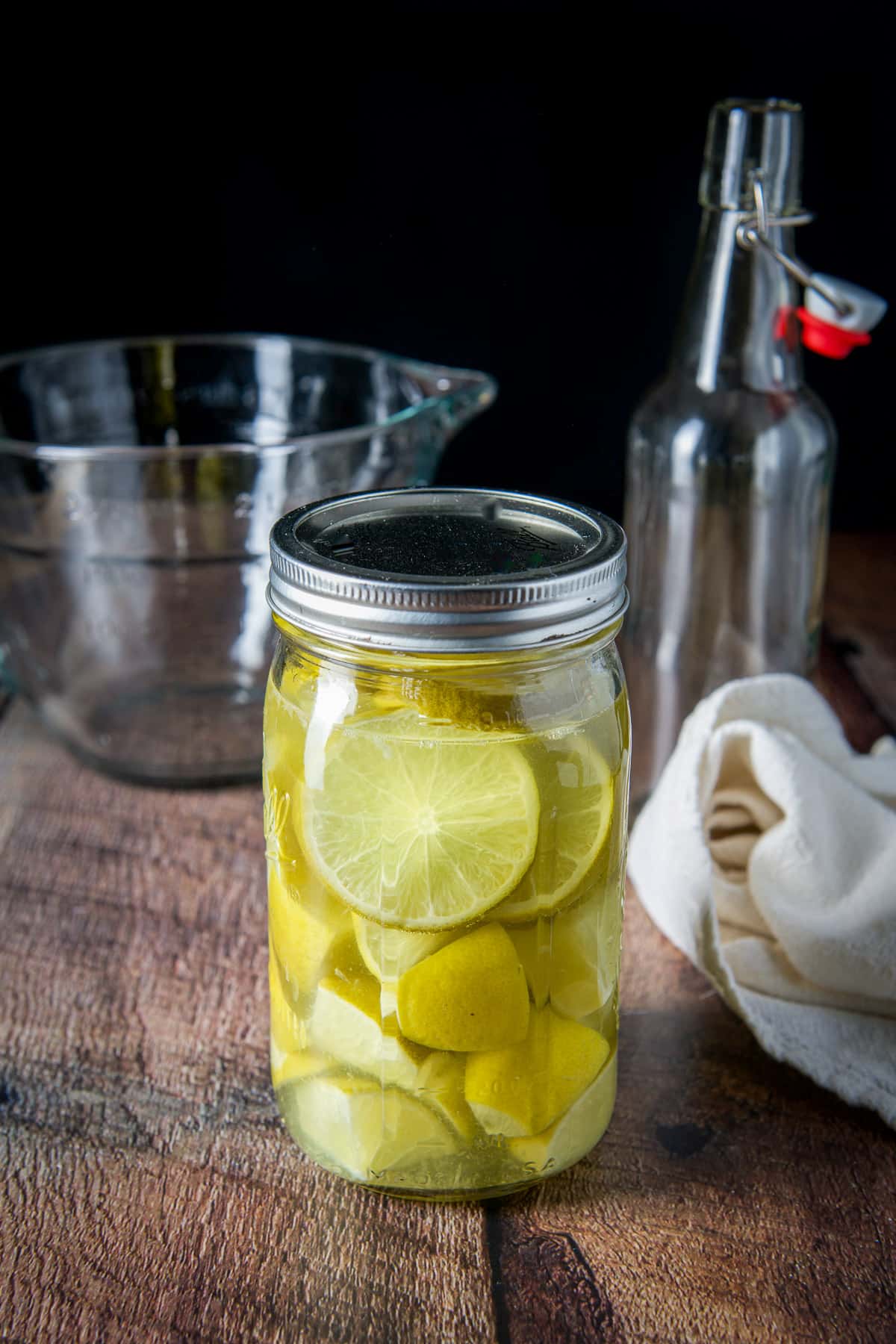 A jar of limes in the vodka with a bowl in the back