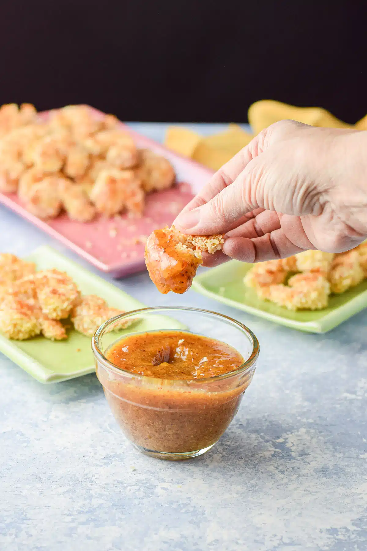A hand holding a shrimp that has been dipped in the sauce