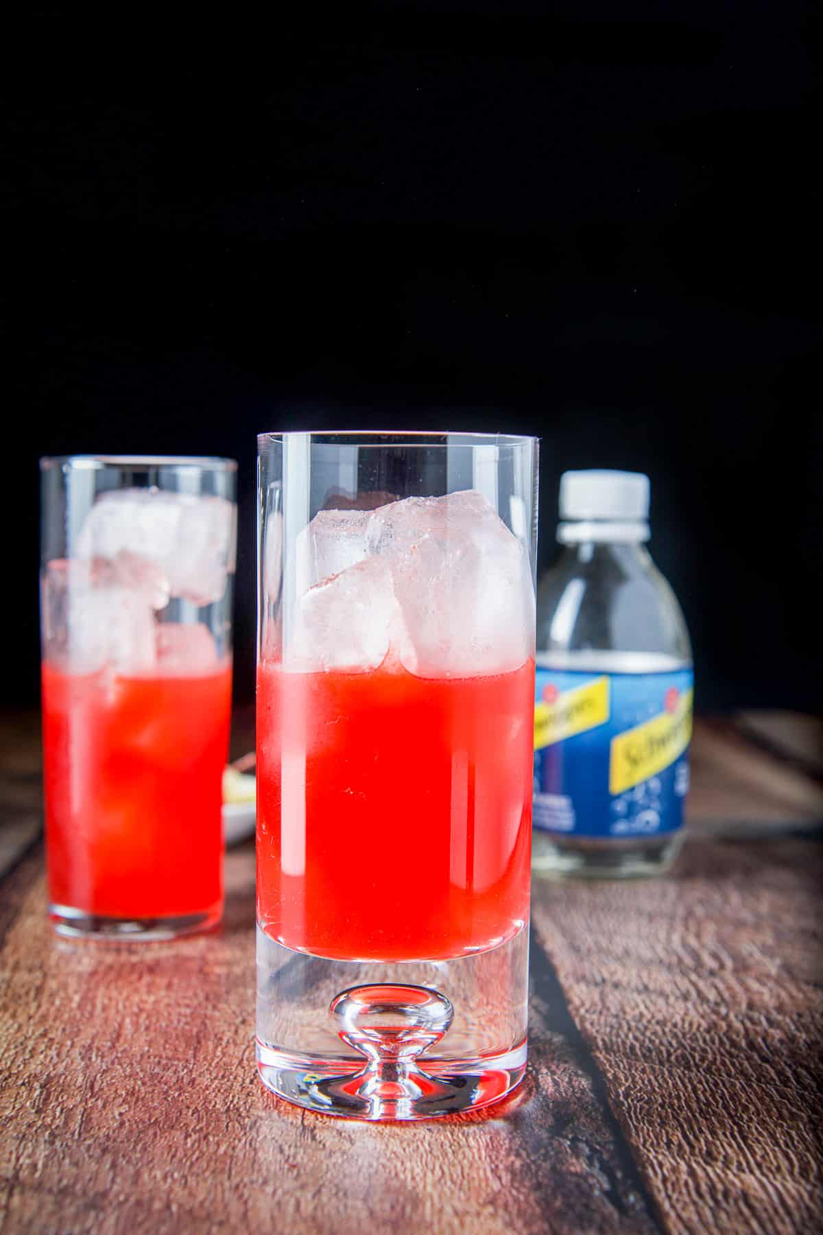 Two tall glasses with ice and the red cocktail poured in it with room for soda