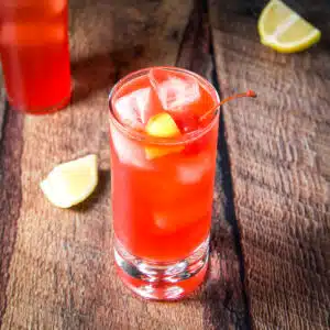 Square photo of a tall glass filled with the red cocktail with lemon and cherry
