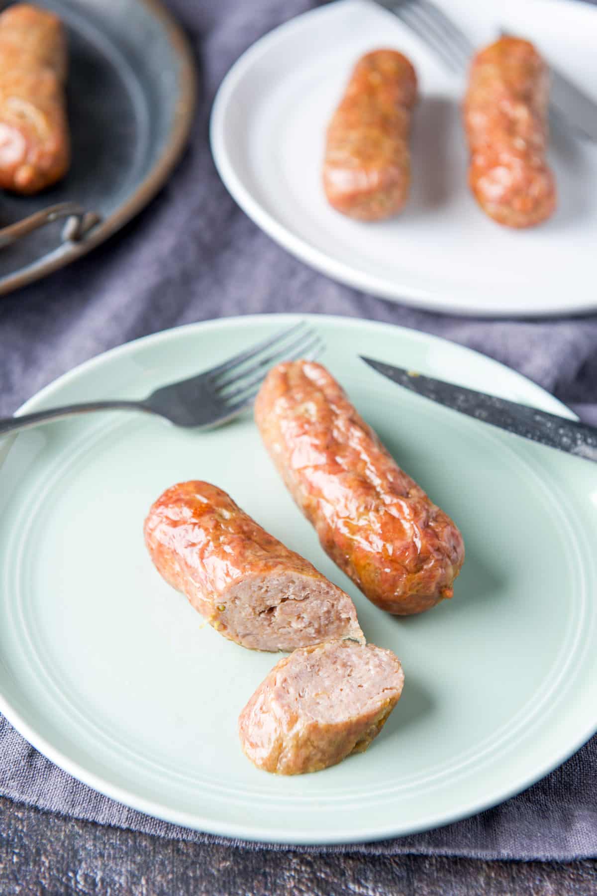 A green plate with two sausages on them, one sausage cut in a few slices