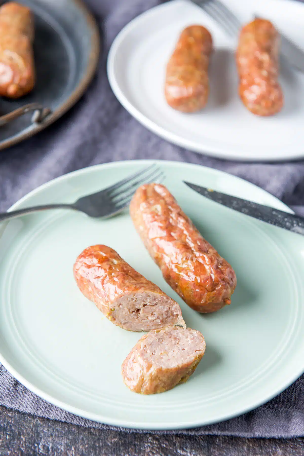 A green plate with two sausages on them, one sausage cut in a few slices
