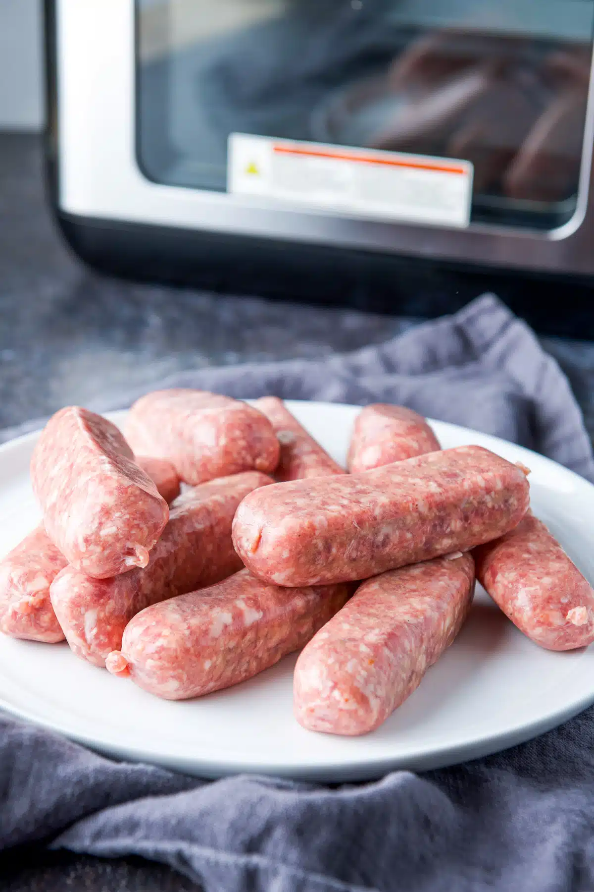 Raw sausages on a plate in front of an air fryer