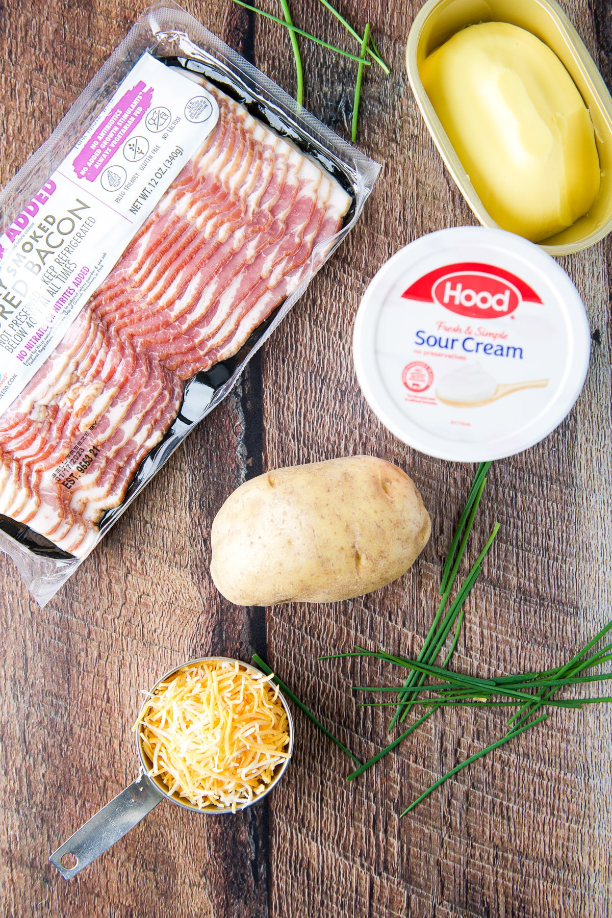 Overhead view of bacon, potato, sour cream, butter, cheese and chives on a table