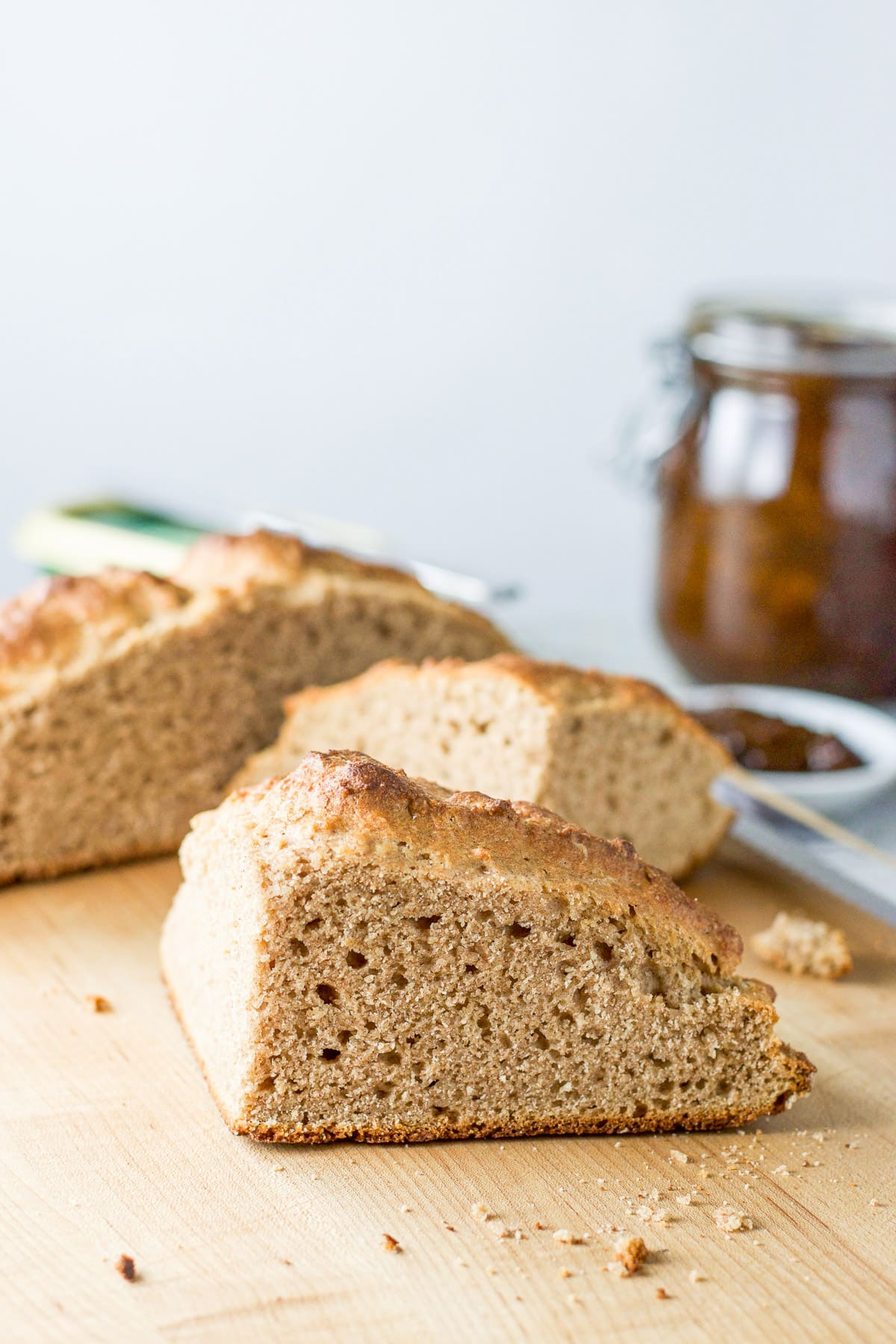 One of the quarters of bread on the board in vertical view with some jam in the back