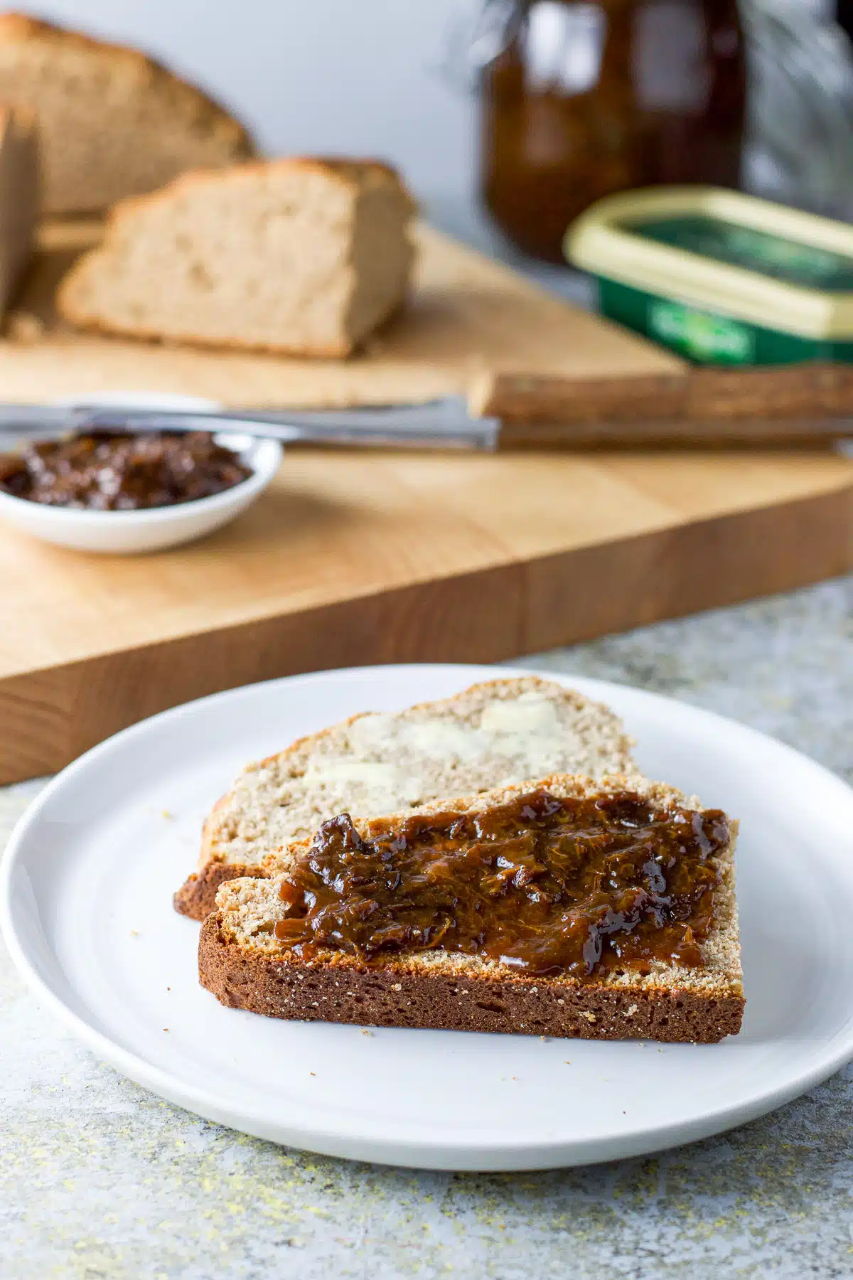 Two pieces of bread with butter and prune spread on it on a white plate with more bread in the back