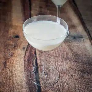A wood table with a bowl glass filled with the white cocktail