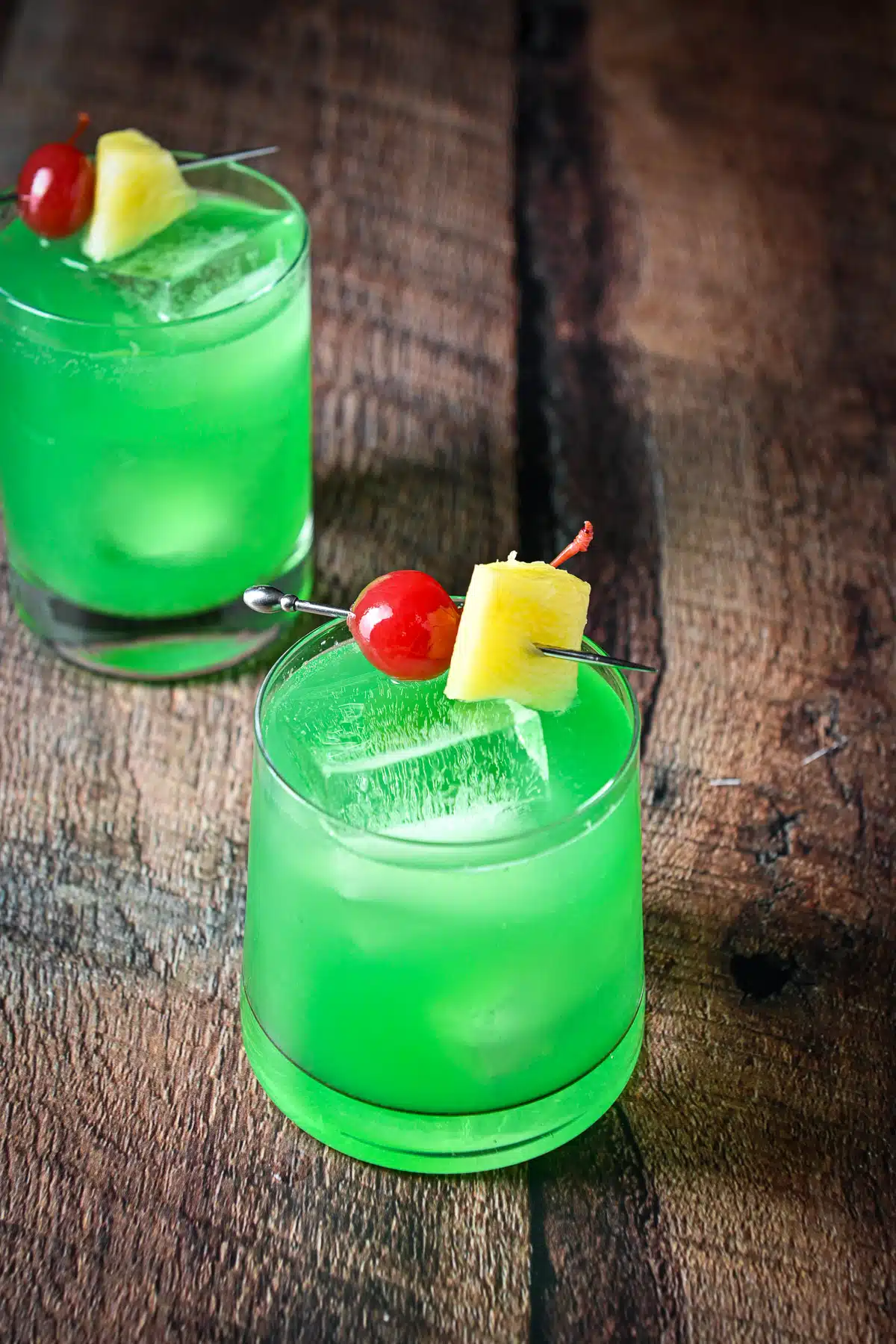 Higher view of the green cocktail with the garnish of cherries and pineapple on skewers