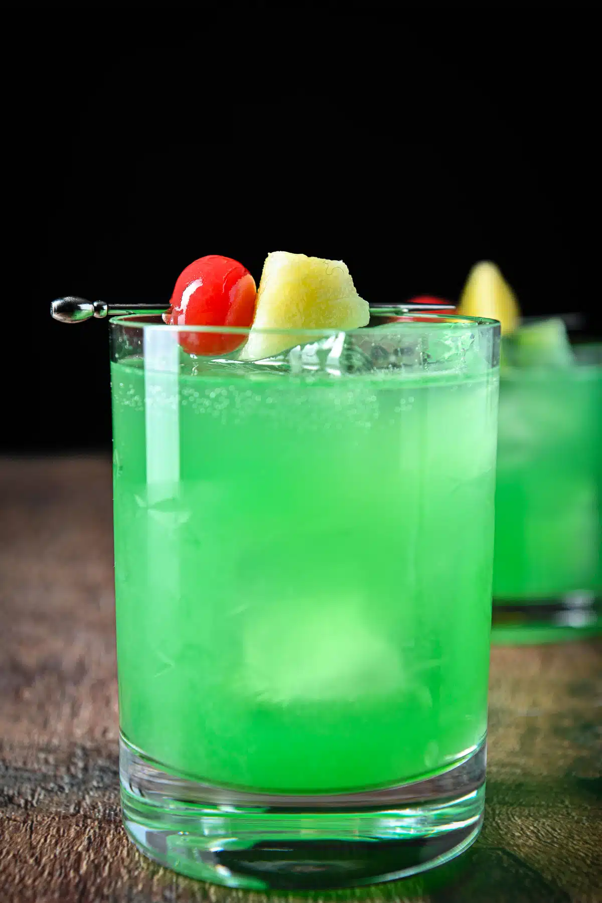 Vertical view of the green whiskey cocktail with cherries and pineapple garnish
