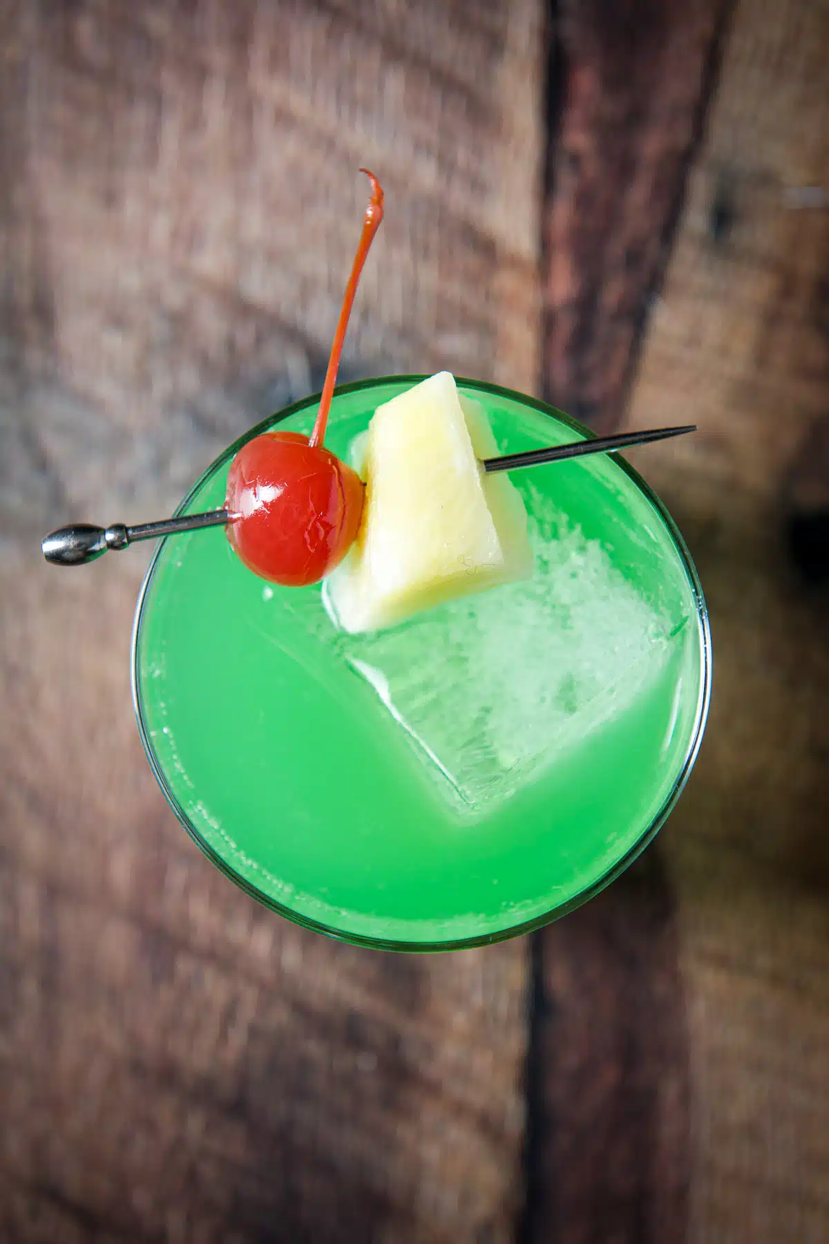 Overhead view of the green cocktail and its garnish of pineapple and cherry