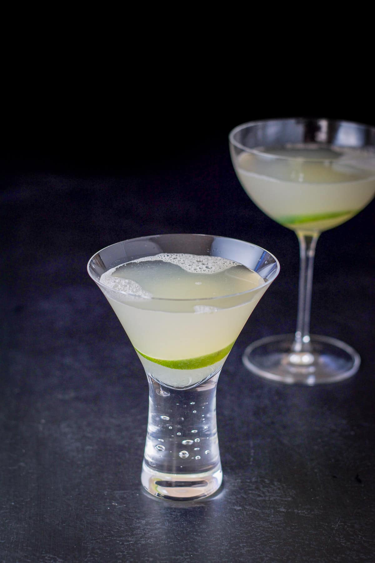 Two glasses filled with a lime cocktail with a lime wheel in each glass
