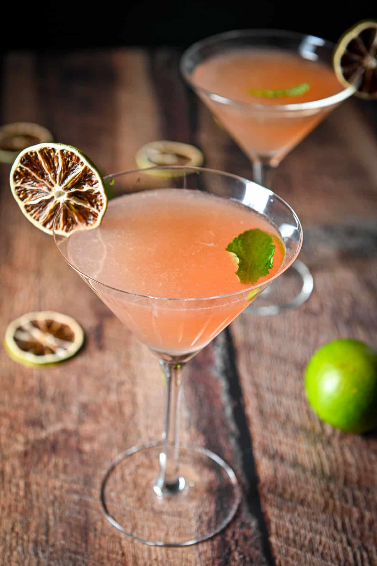Two martini glasses with the berry drink with limes and mint as garnish