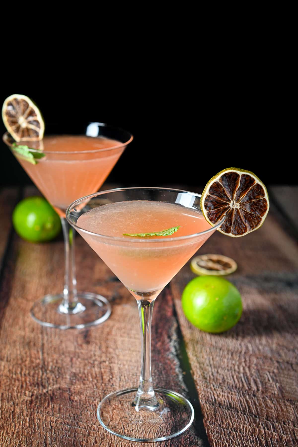 Two martini glasses with the blackberry drink in them and limes and mint as garnish