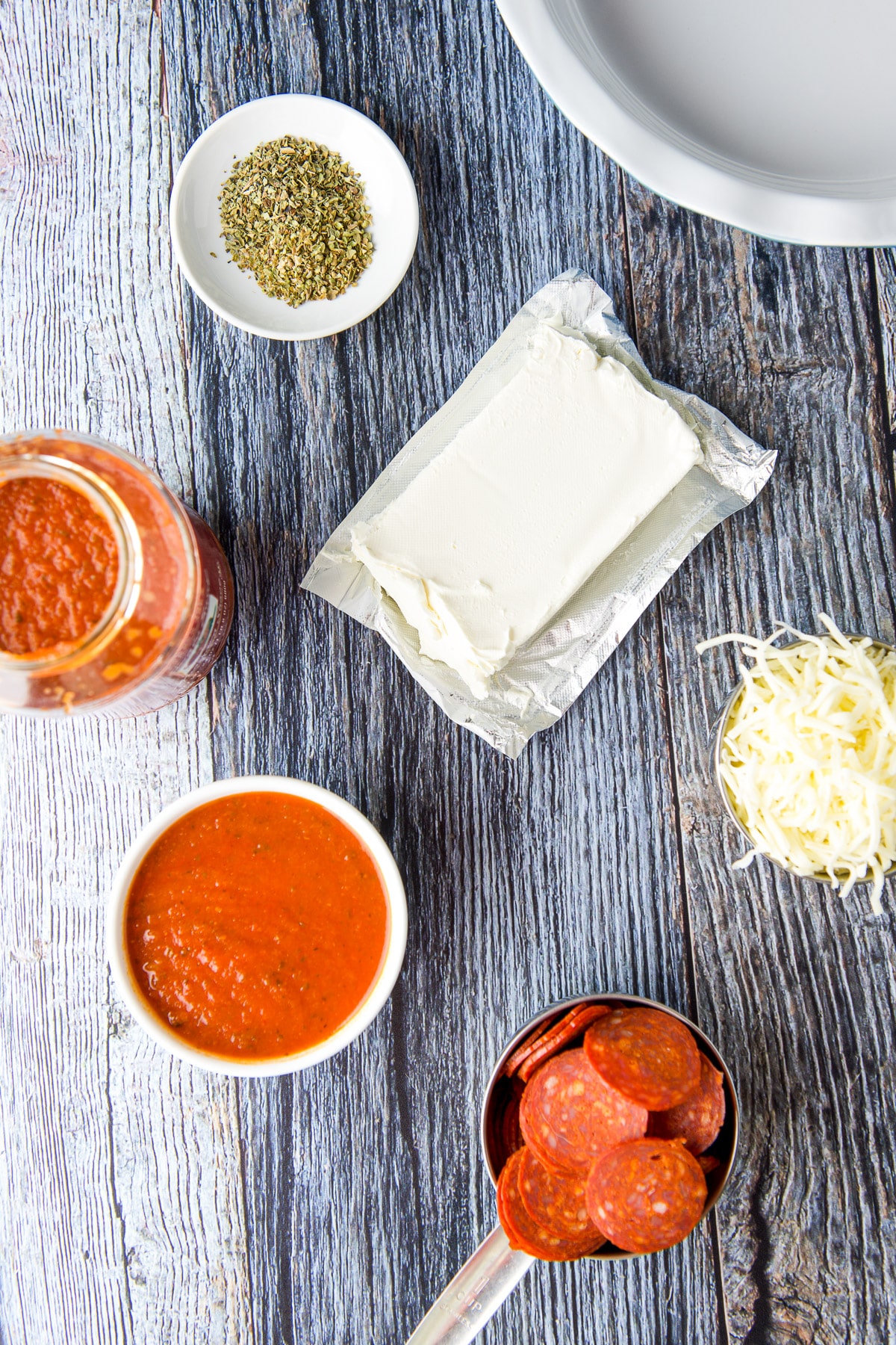 Cream cheese, mozzarella cheese, pasta sauce, pepperoni slices and herbs on a table