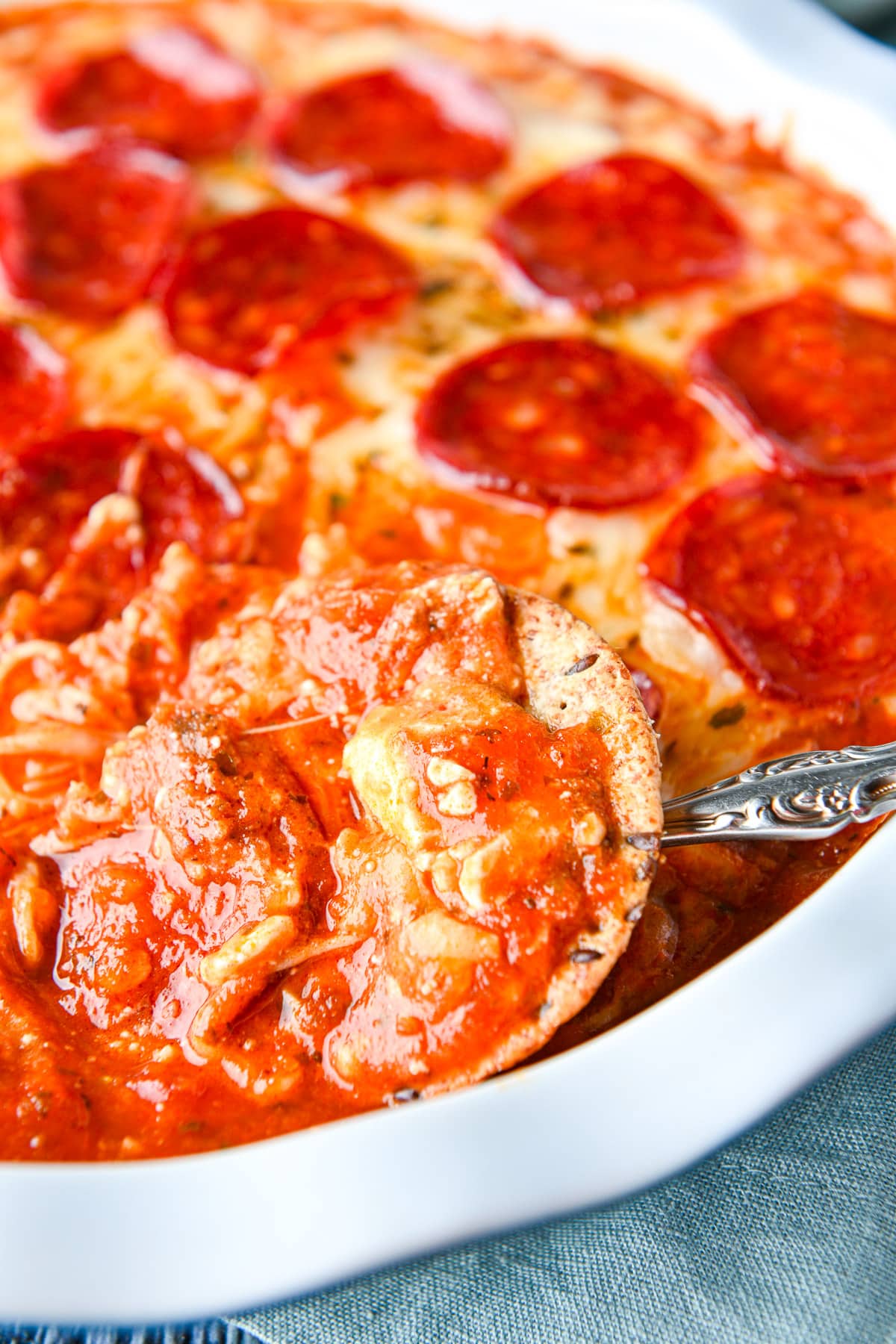 A cracker in the dip with pasta sauce and pepperoni