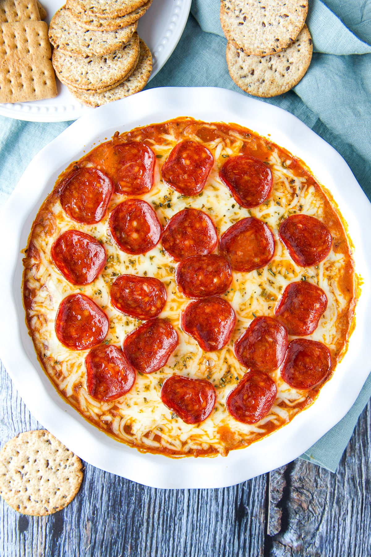 Overhead view of the pizza dip in a pie plate with crackers strewn on the table