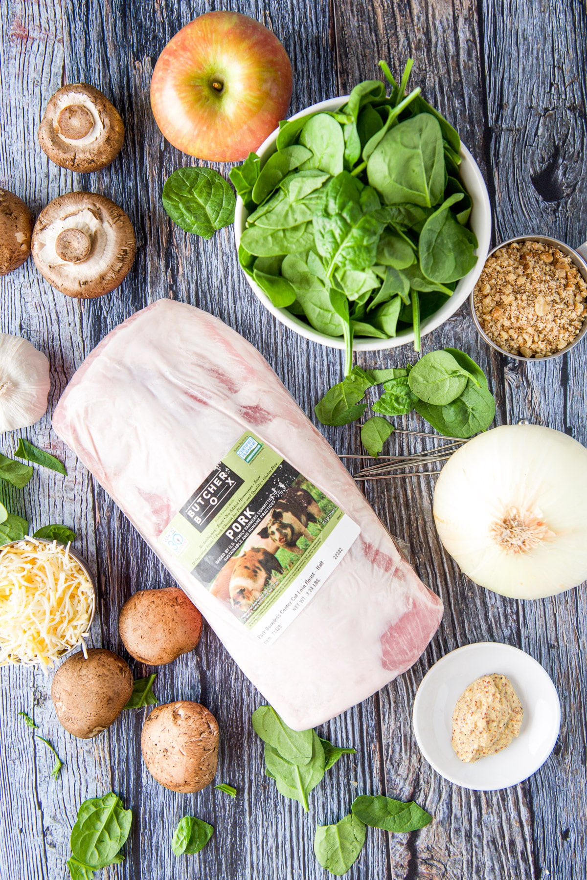 Pork loin, spinach, onion, mustard, mushrooms, walnuts, apple, garlic and cheese on a table