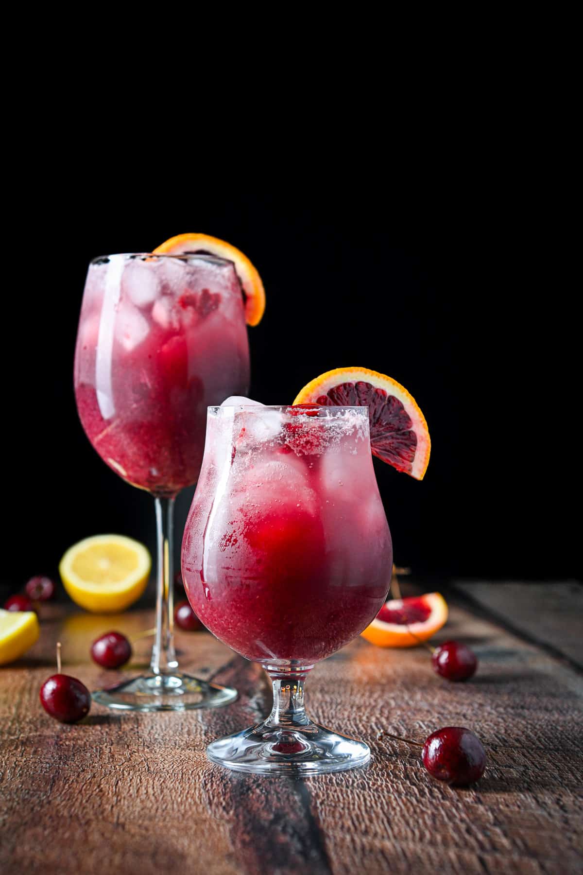 vertical view of the tulip glass and wine glass filled with the wine drink, garnished by orange slices with cherries and other fruit on the table