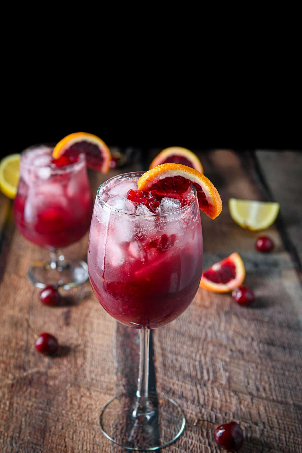 The tall wine glass in front of the shorter glass with blood orange slices on the rim for garnish