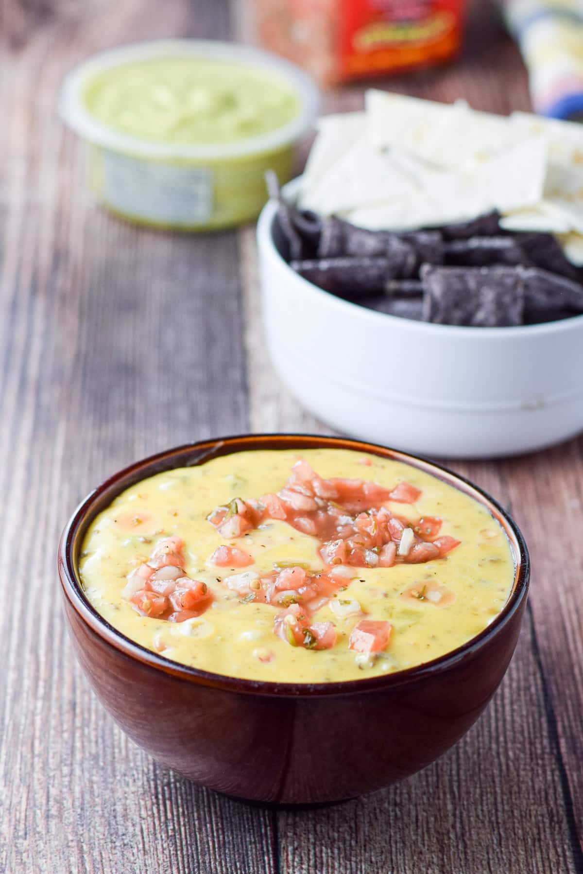 A brown bowl with the dip in it with chips and guac in the back