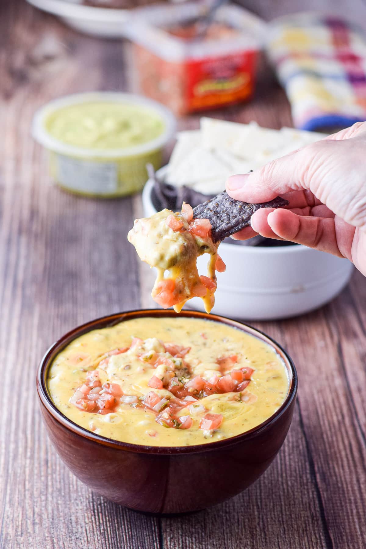 A hand holding a chip that was dipped in the cheese dip