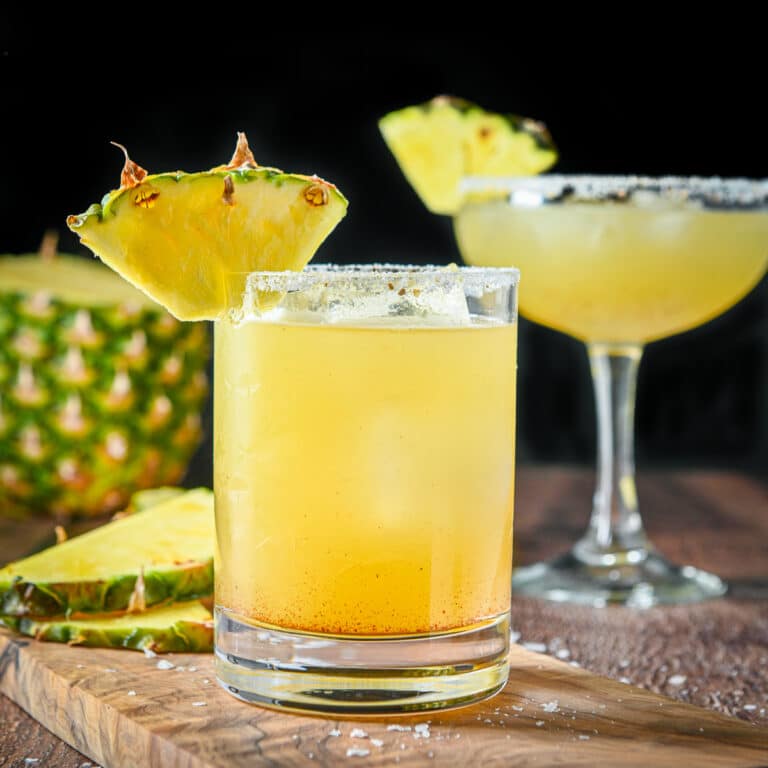 square photo with two margarita glasses filled with the margarita with pineapples on the rims and more on the table