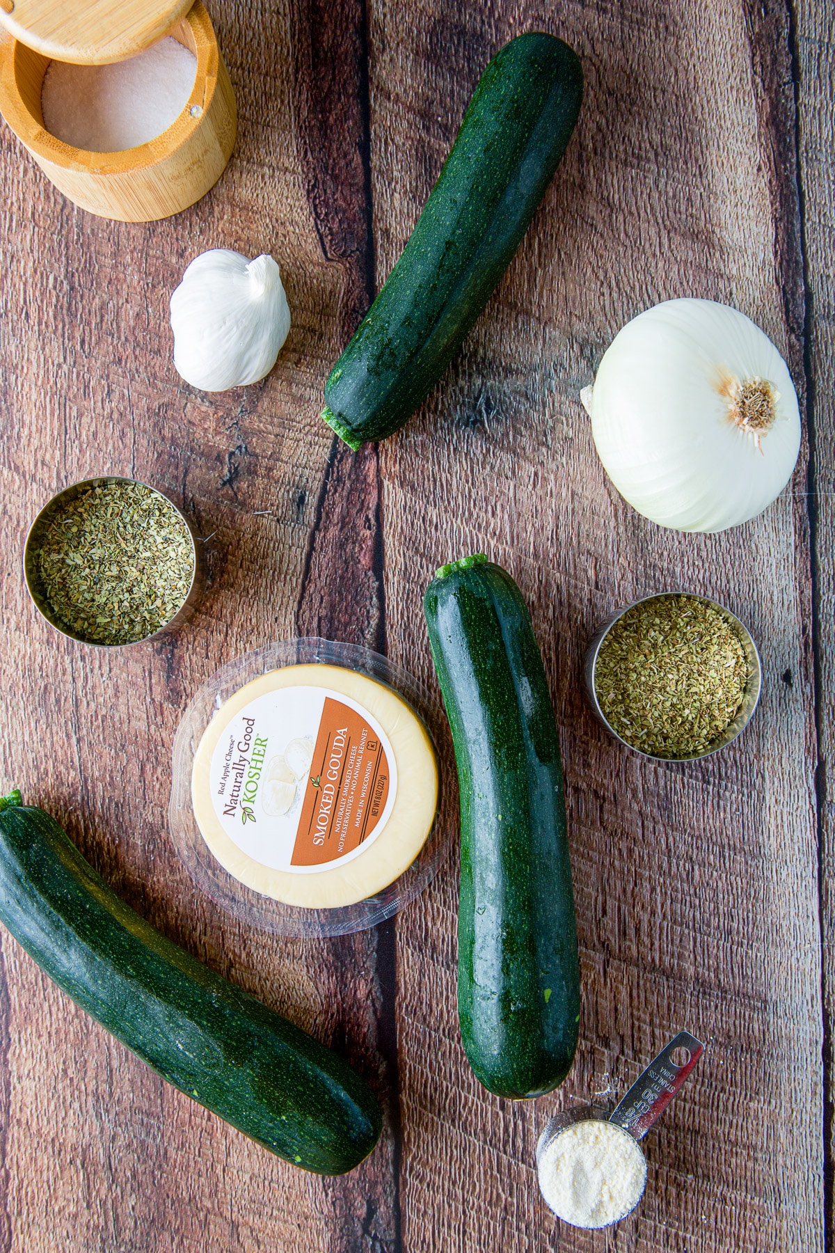 A table with zucchini, gouda cheese, onion, garlic, parmesan cheese, herbs, and salt
