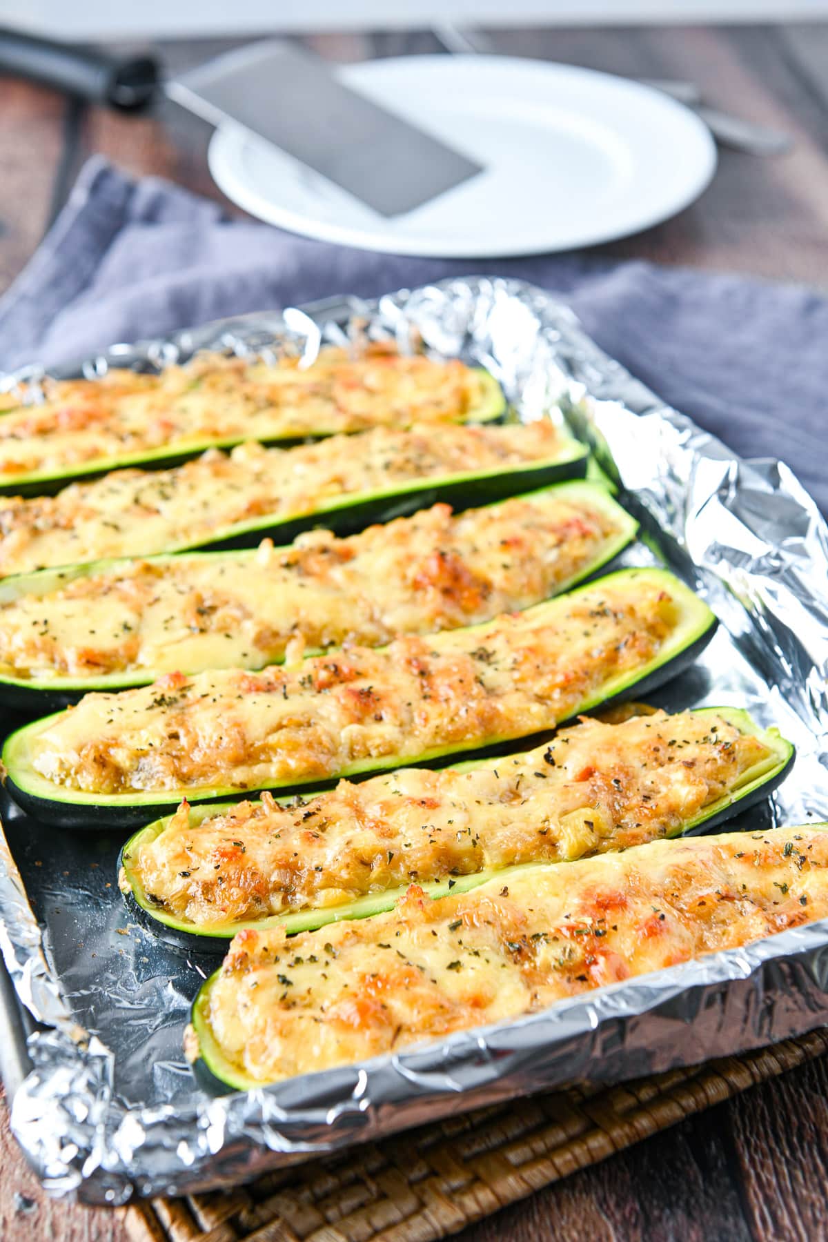 The cooked zucchini on the foil lined pan with a white plate and spatula on it