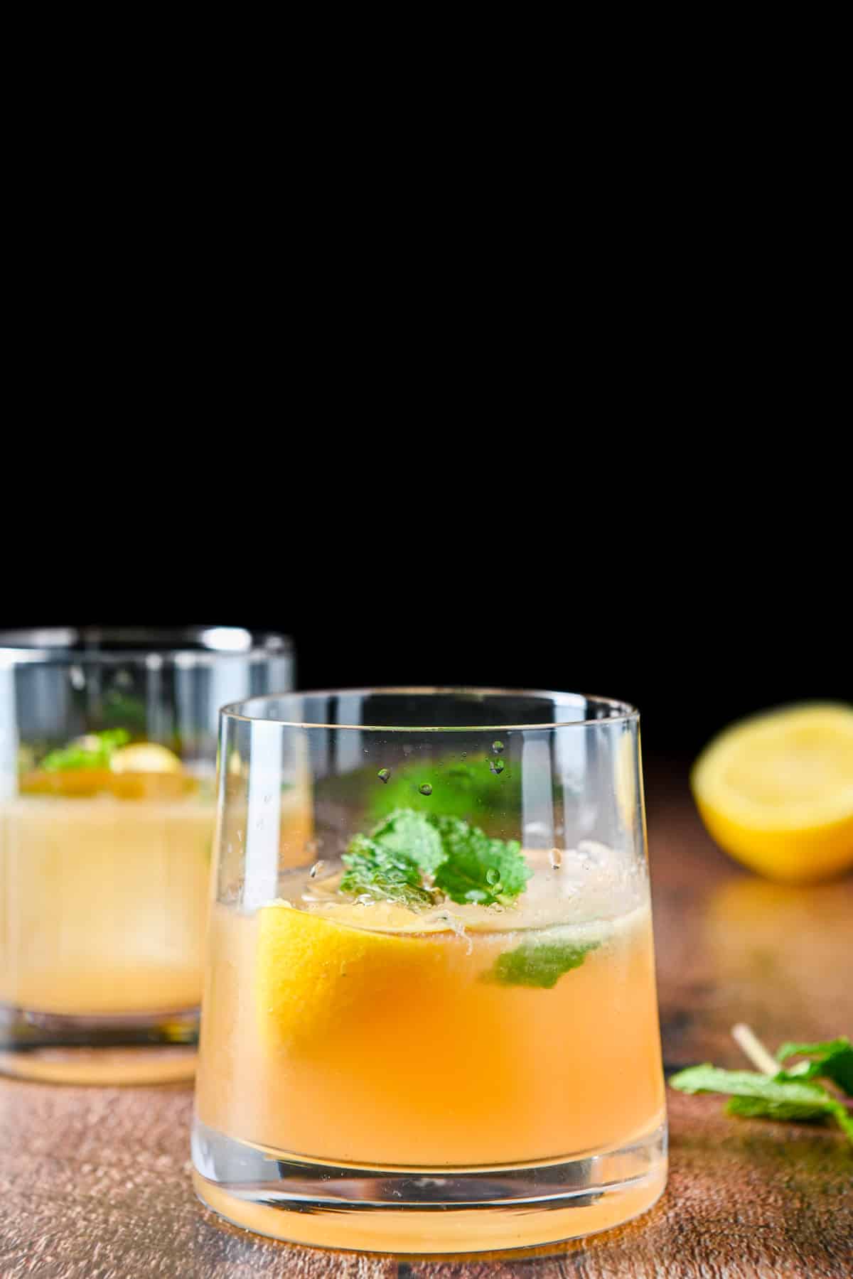 A sloped glass with the whiskey drink with lemon and mint in front of another