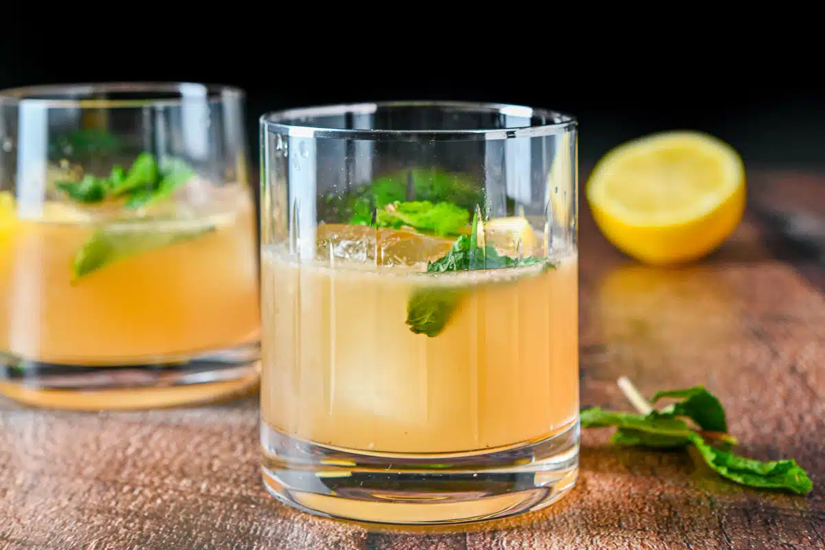 two glasses with the bourbon cocktail it it with mint and lemon as garnish - horizontal