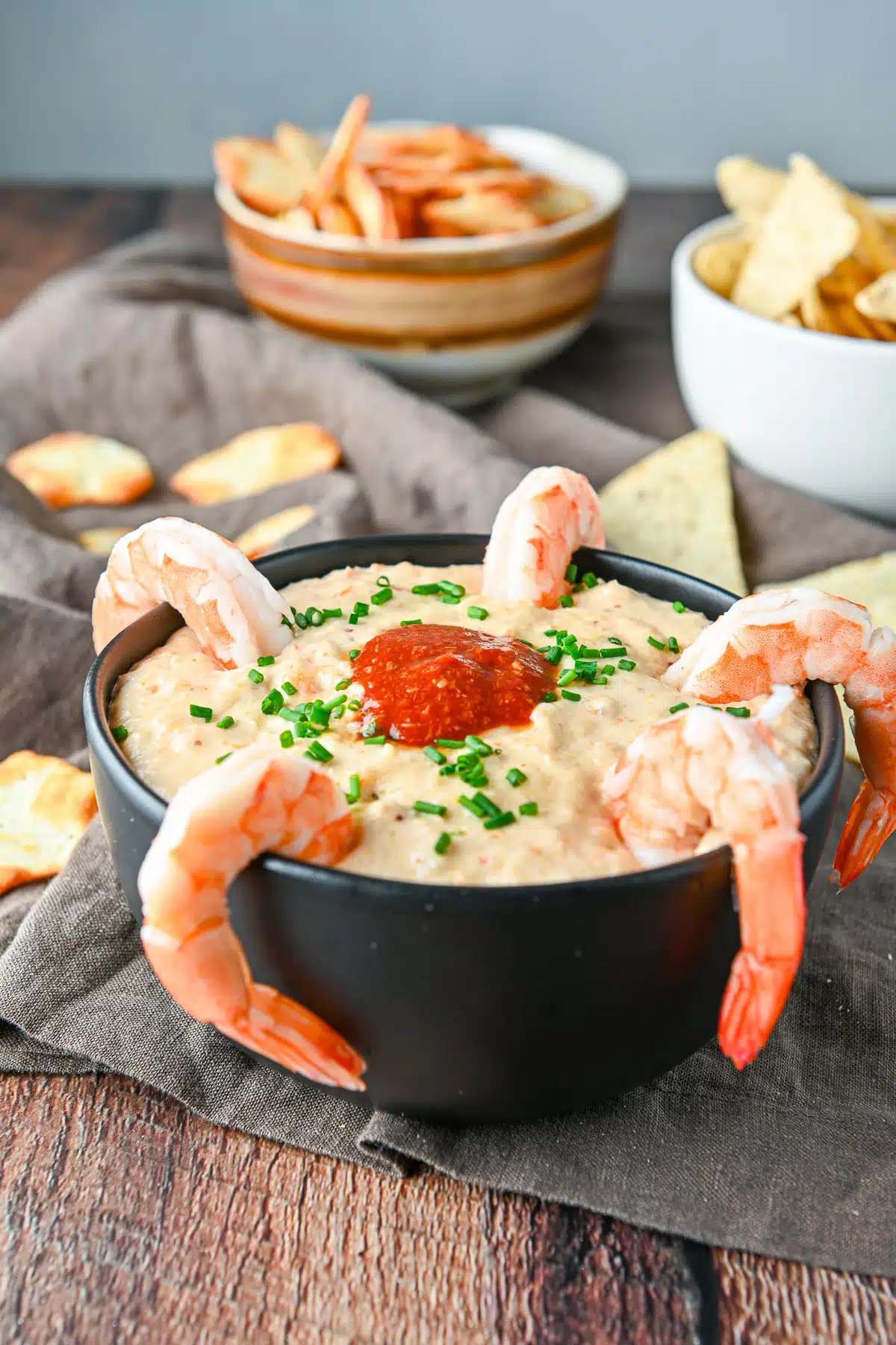 A black bowl filled with the dip with shrimp on the rim and cocktail sauce on the dip