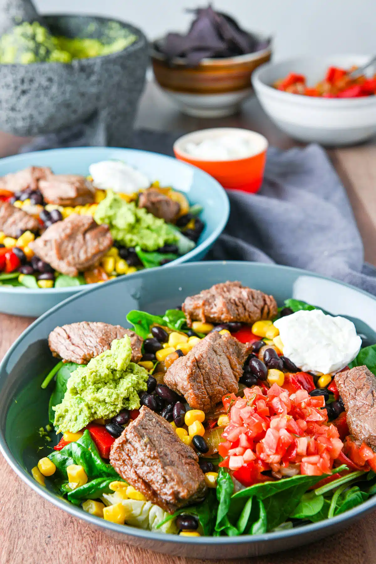 Steak on the vegetables, along with condiments in bowls with chips, sour cream, and guacamole behind them