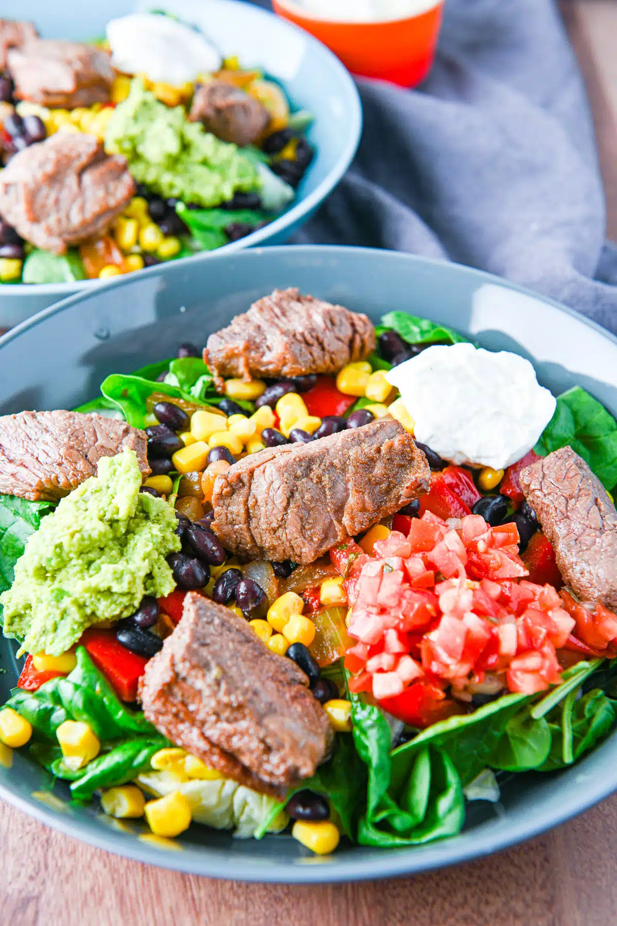 Close up of two steak bowls with vegetables, sour cream, guacamole, and salsa