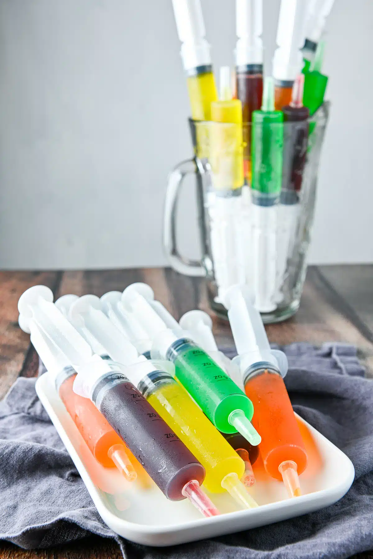 Syringes filled with different kinds of jello on a plate and in a pitcher