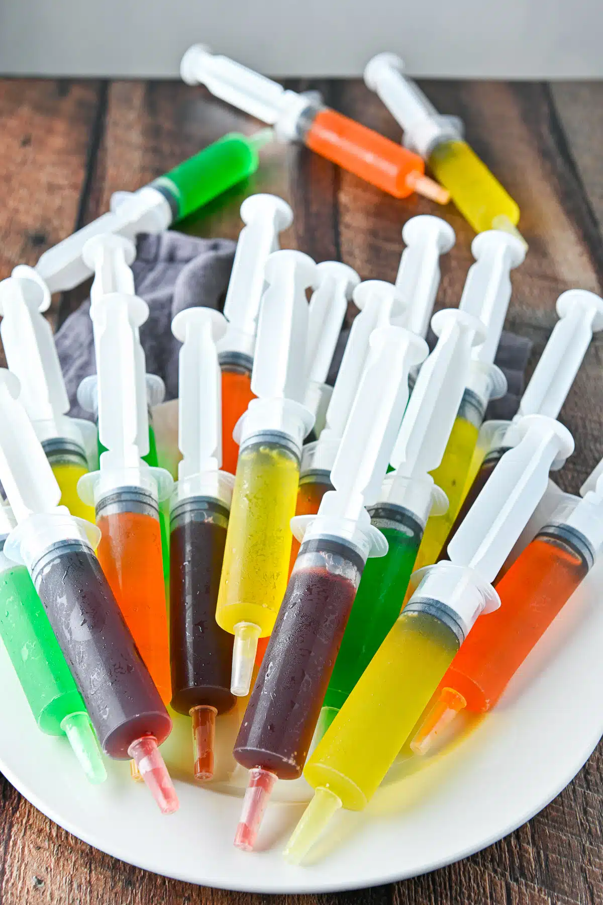 A pile of jello filled syringes on a plate with more in the back