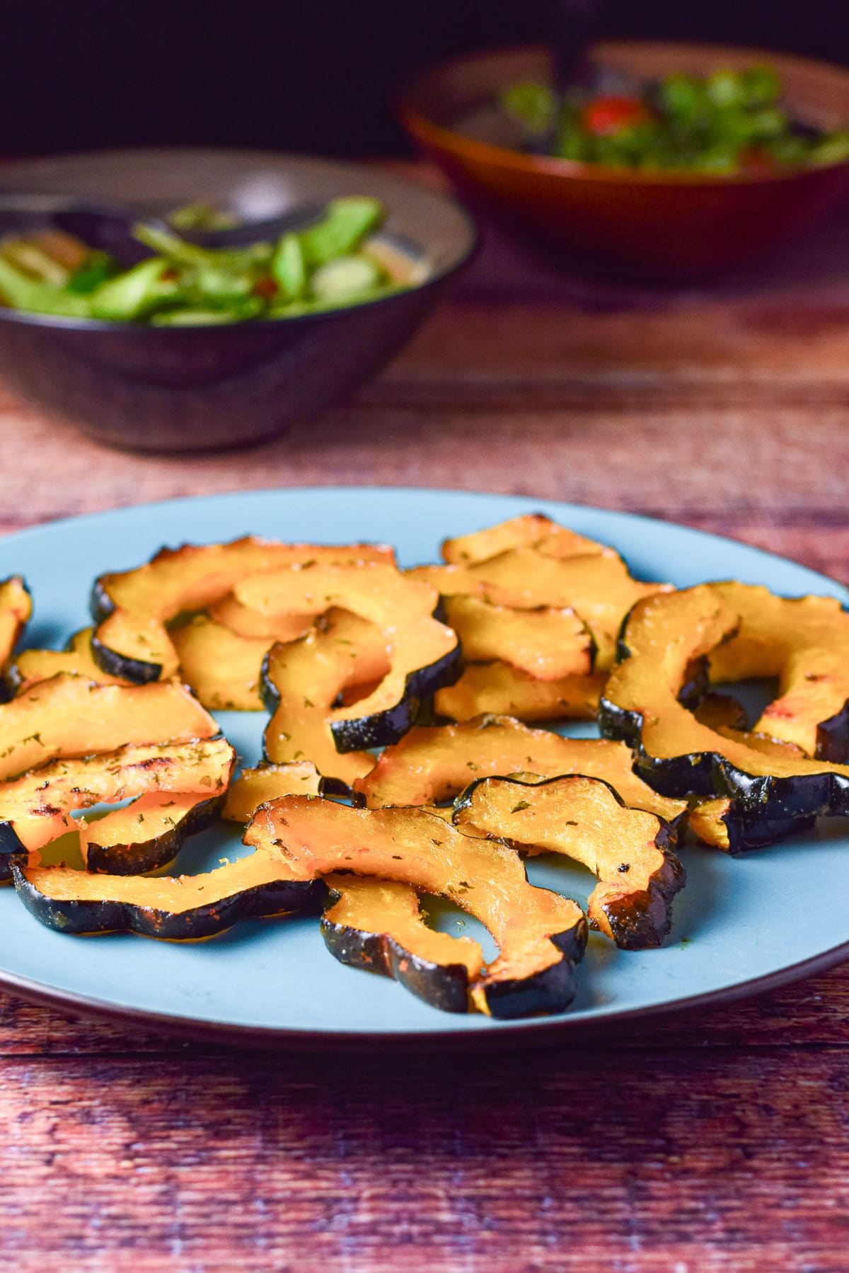 sliced squash on a blue plate and two salads in the background