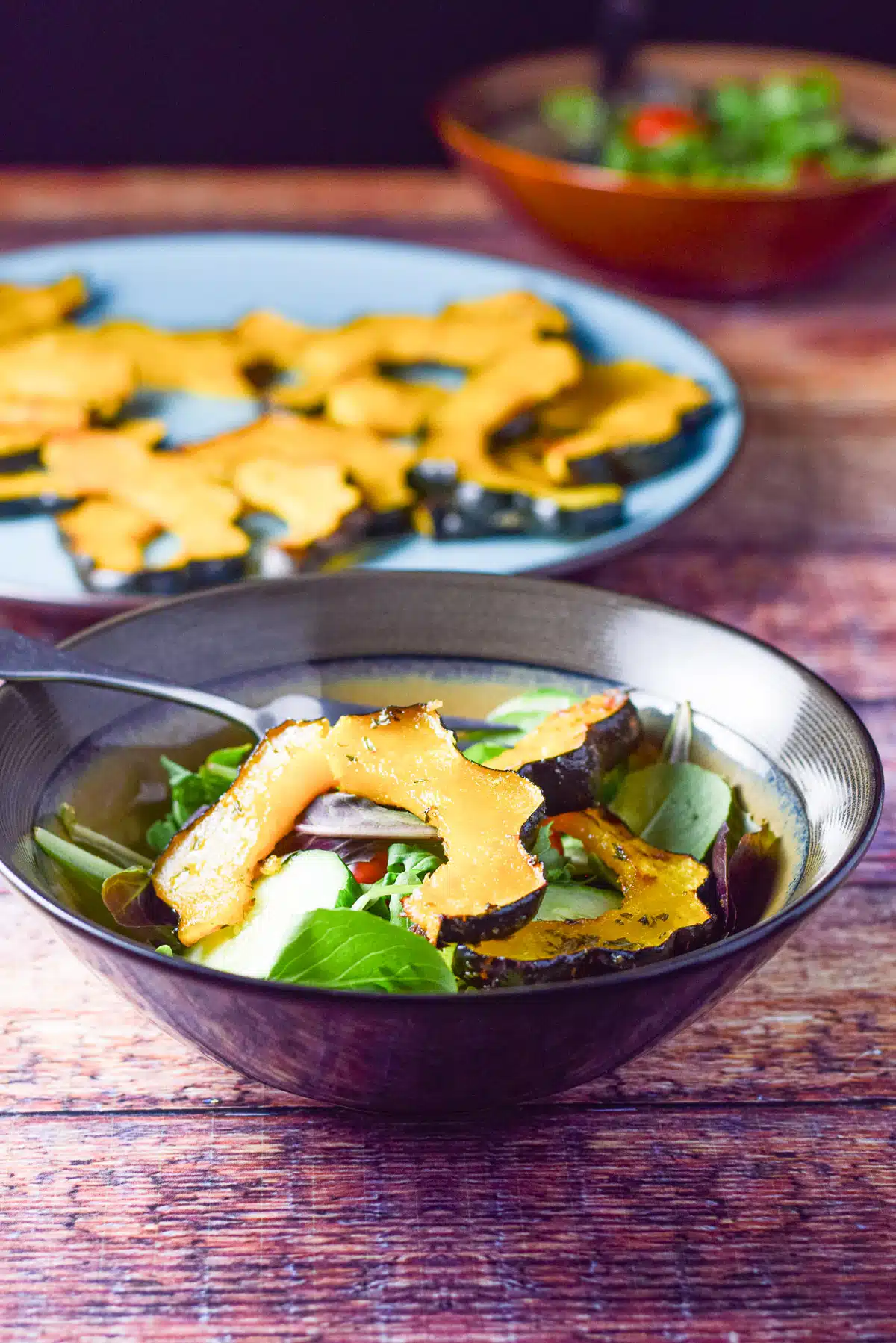 acorn squash on a salad with another salad in the background along with a plate of the vegetable