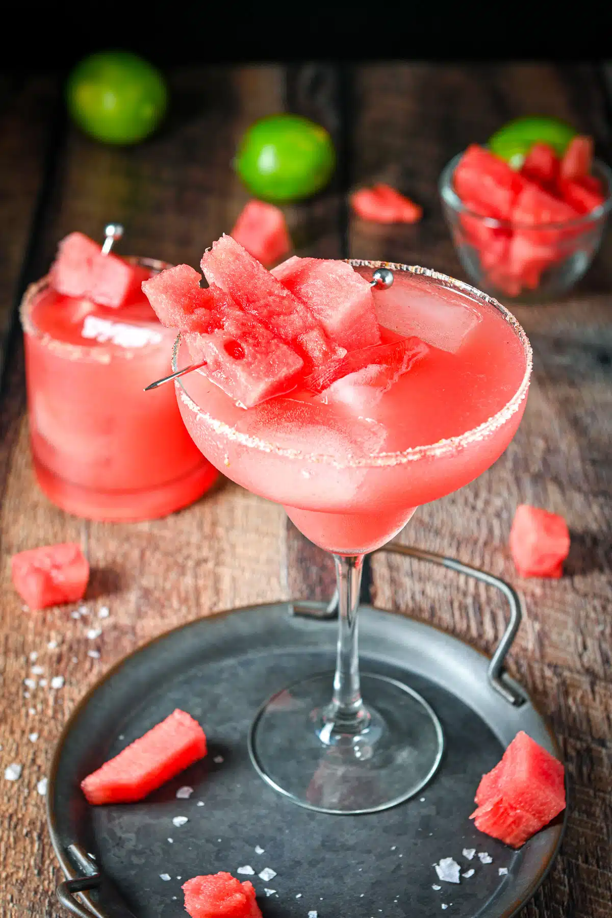 Watermelon on a pick in the margarita with more watermelon and limes in the back