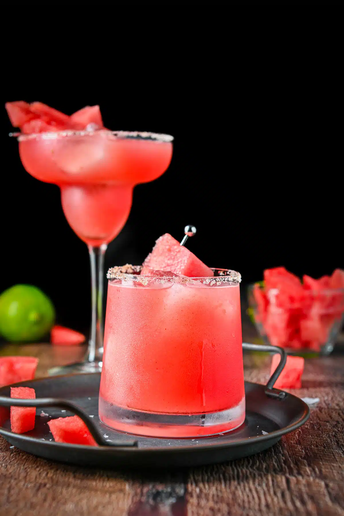 Vertical view of the margarita in a short and tall glass with watermelon and lime in the back
