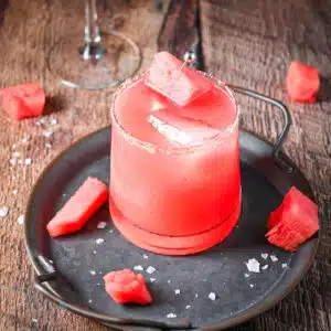 A metal tray with the watermelon drink on it with chunks of watermelon and salt