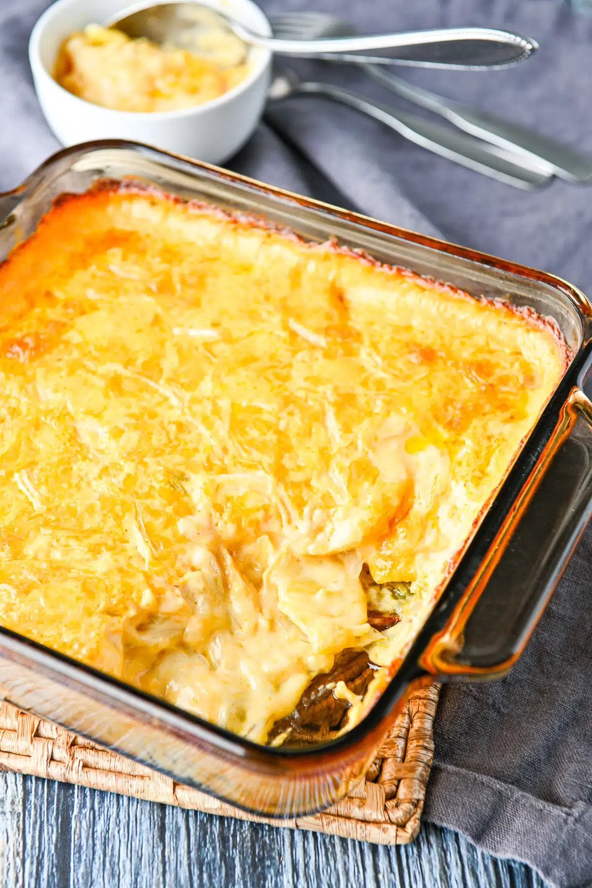 A casserole dish with the potato casserole all creamy with a white bowl behind with more in it