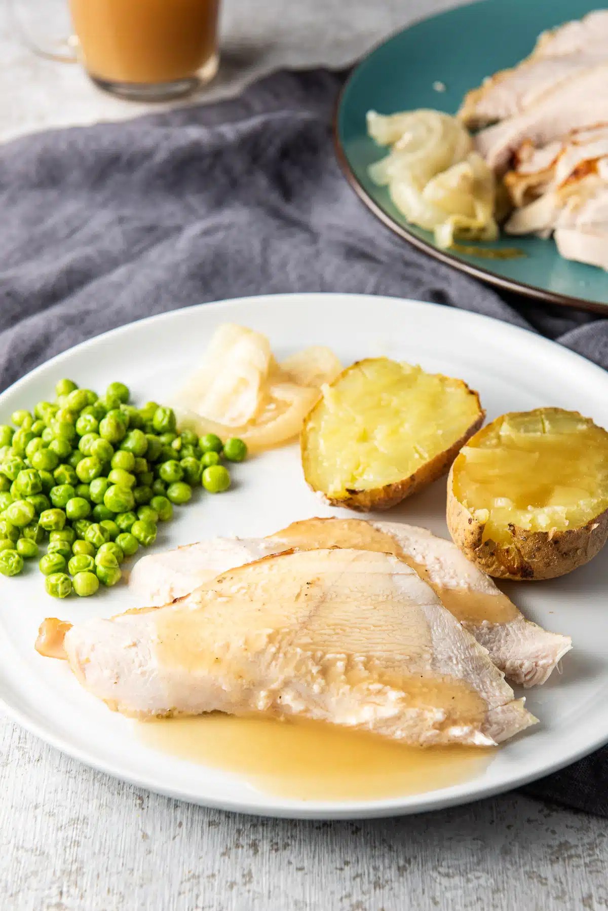 A white plate with two pieces of turkey on it with peas, potatoes, and onion