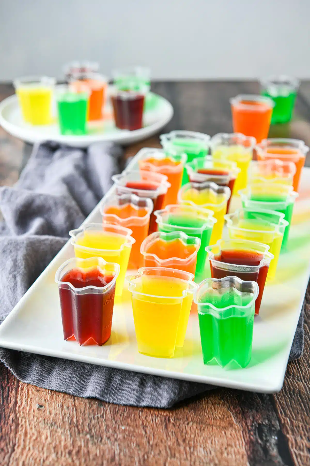 A white rectangular platter with multi colored jello shots in cups