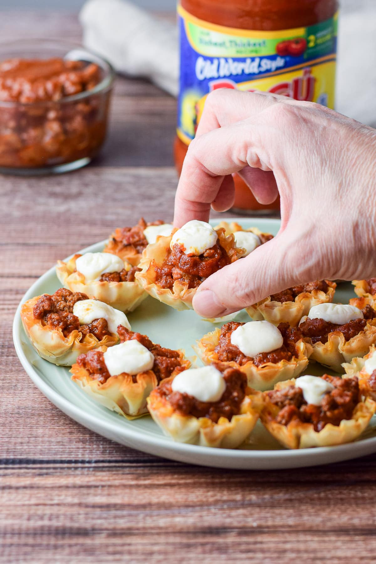 A woman's hand holding one of the beef appetizer's over the plate of the appetizer