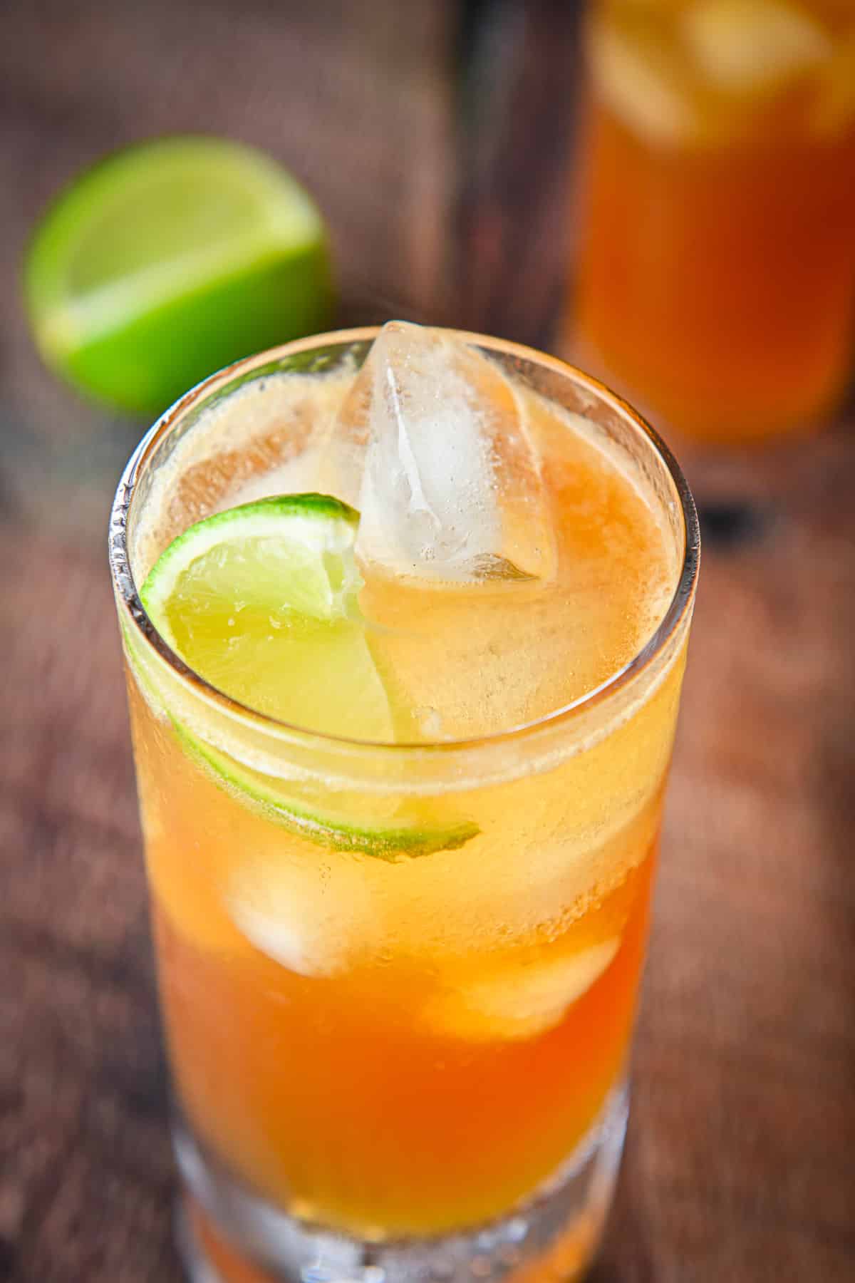 Close view of the cocktail with the lime wedge in it along with more lime and another glass in back