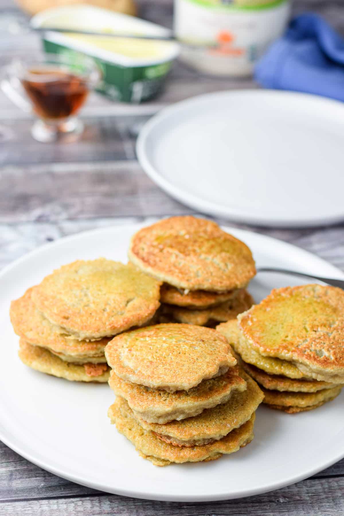 a large white plate with stacks of pancakes on it with butter, syrup, and another plate behind